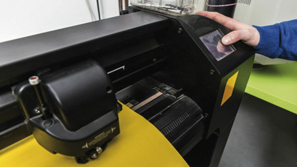 Beschriftungsdesign und Werbetechnik – Lehrling bedient eine Druckmaschine